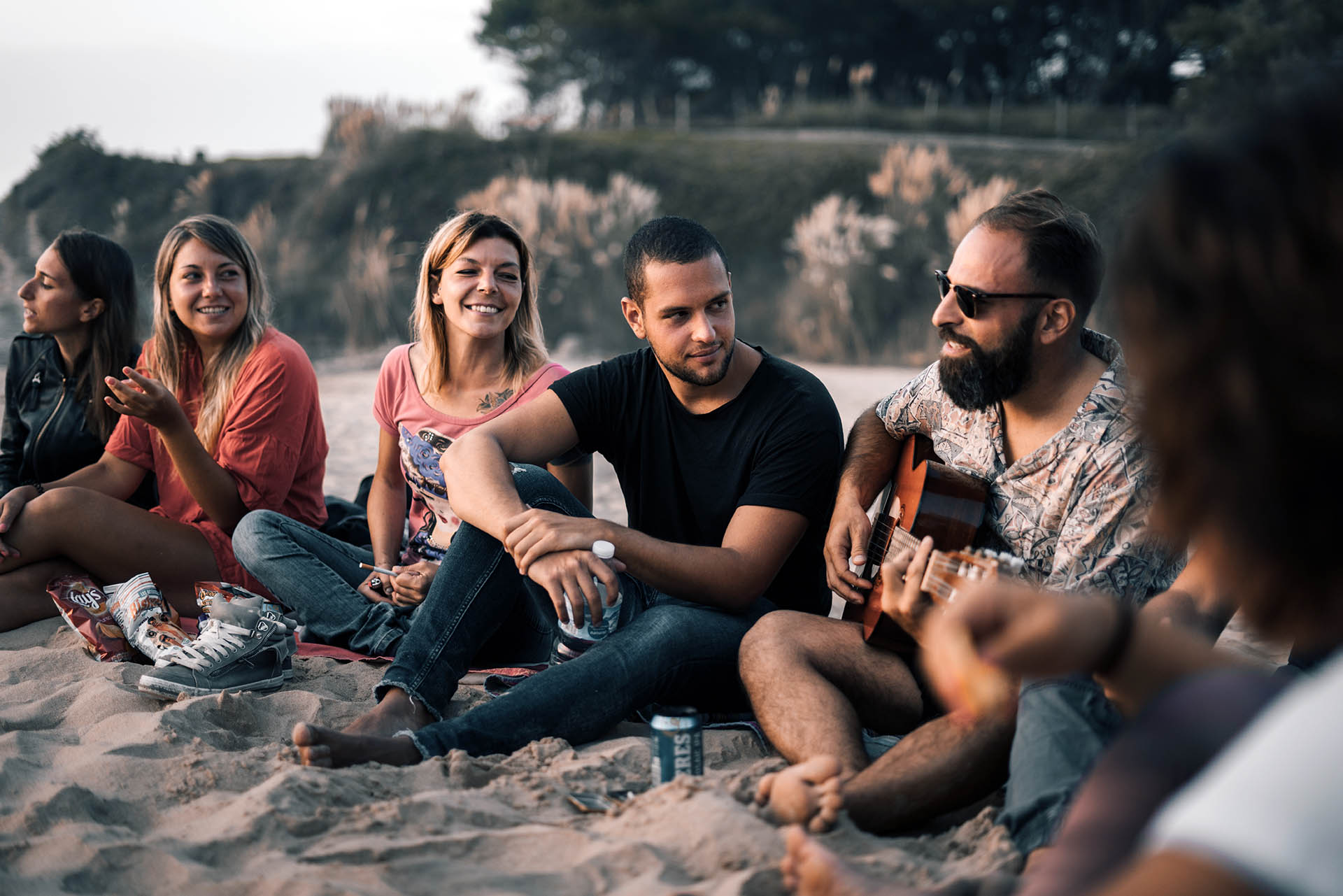 Ragazze e ragazzi di una SurfWeek seduti in cerchio sulla sabbia nella luce del tardo pomeriggio, uno suona la chitarra
