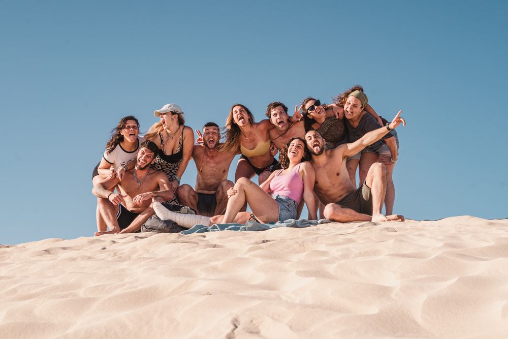 Un gruppo SurfWeek abbracciato in cima a una duna di sabbia a Fuerteventura, sotto il cielo azzurro