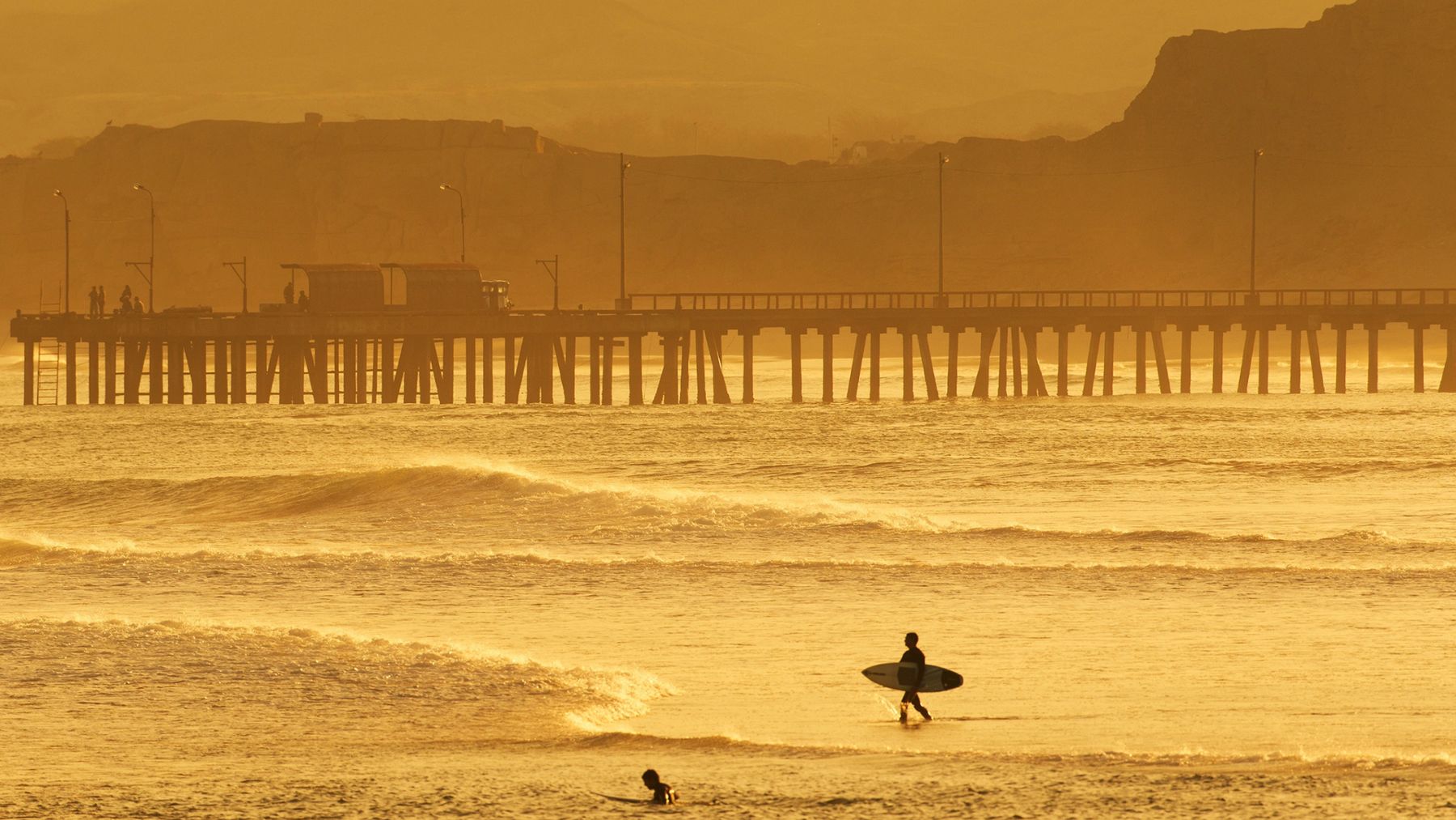 Il molo di Huanchaco al tramonto con un surfista sulla spiaggia