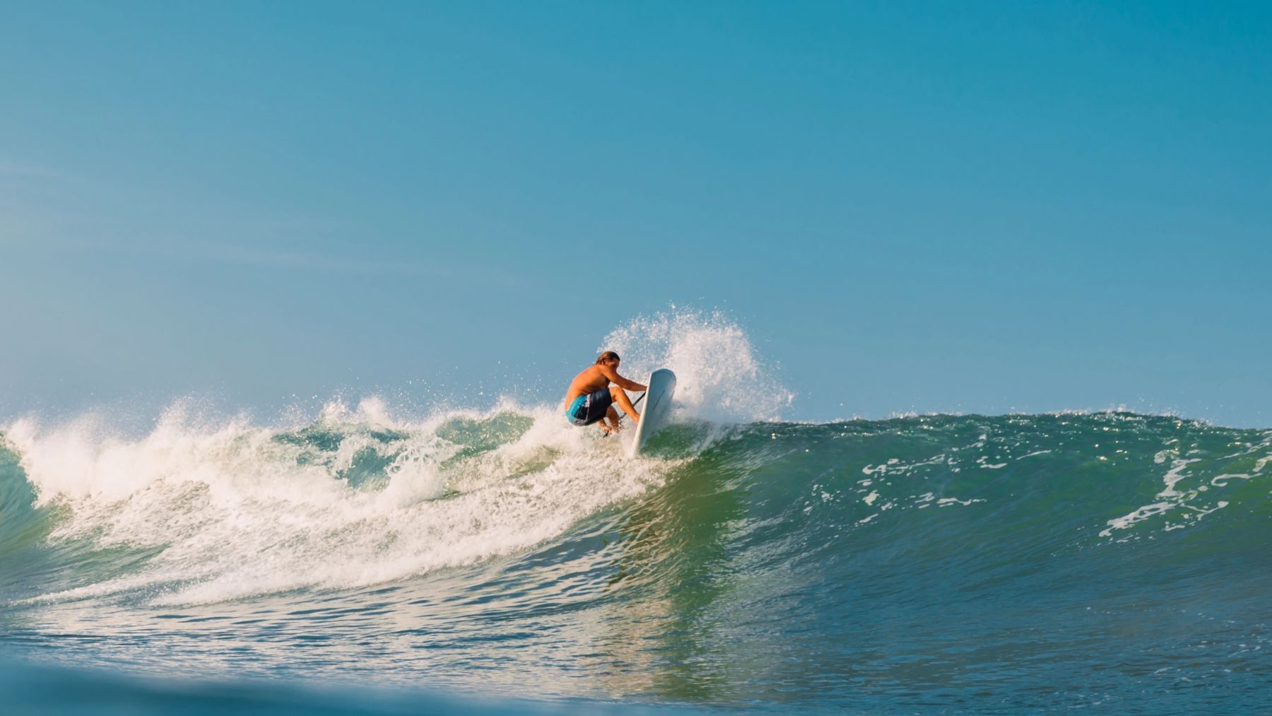 Un surfista in piedi sulla parete di un'onda azzurra