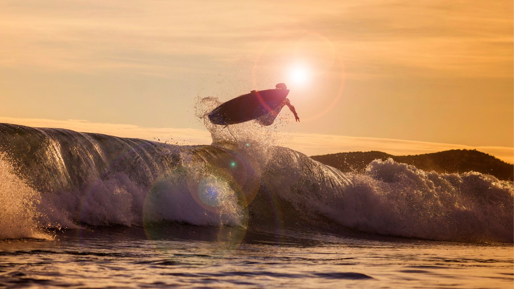 Un surfista vola sopra la cresta di un'onda contro il sole basso